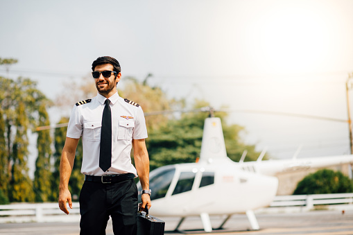 Portrait of helicopter pilot in uniform walk and standing outside with private helicopter background