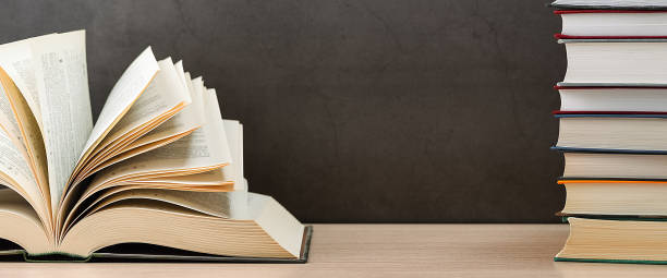istock The book is open, the sheets are fan-shaped on a black background next to a stack of books. 1261031316