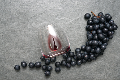 Wine Glass with red wine and black grapes on stone table surface flat lay background.