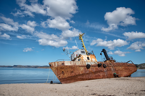 Rusty old abandoned iron fishing boat which is pulled out on the coast of the sea in Teriberka