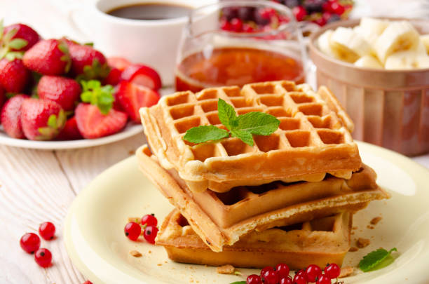 istock Stack of three belgian waffles on white kitchen table with strawberries bananas syrup coffee and red currant 1261109036