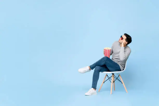 Photo of Young Caucasian man holding popcorn and 3D movie glasses looking up