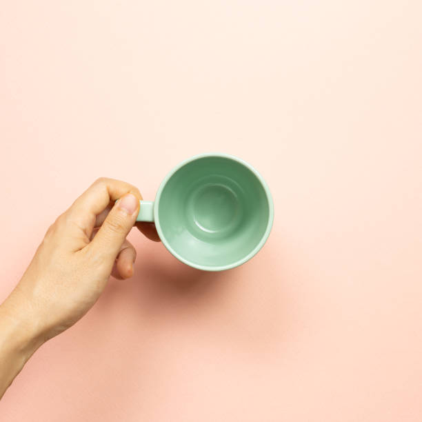 istock Female hand holding green empty mug cup on pink background. top view 1261129020
