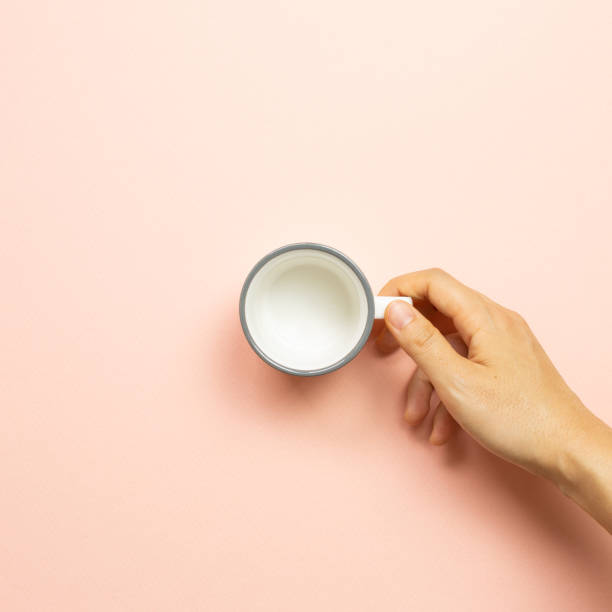 istock Female hand holding white empty mug cup on pink background. top view 1261129522