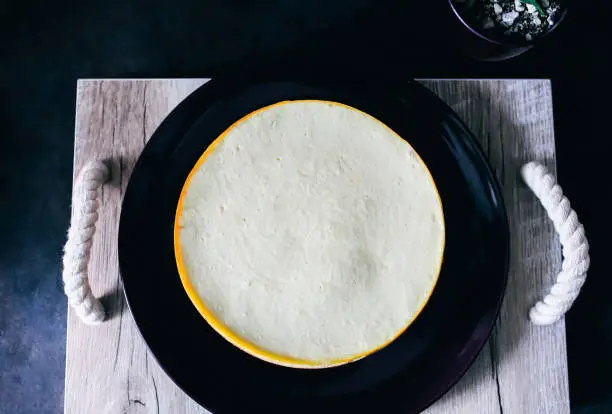 Homemade vanilla New York cheesecake on the dark-purple plate and wooden tray with rope handles. Succulent is nearby. Dark-violet, petunia and grey hygge kitchen colors. Rustic and classical dessert.