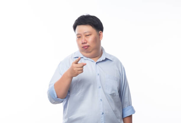 Young Fat Asian business man poiting to camera with funny face isolated on white background Young Fat Asian business man poiting to camera with funny face isolated on white background. business person one man only blue standing stock pictures, royalty-free photos & images