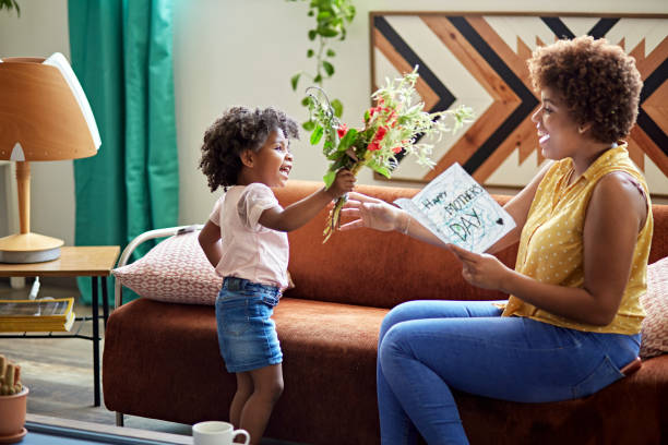 Child Expressing Gratitude and Love on Mother’s Day Side view of 3 year old Afro-Caribbean girl giving mother in mid 20s bouquet of flowers and homemade card. candid bonding connection togetherness stock pictures, royalty-free photos & images