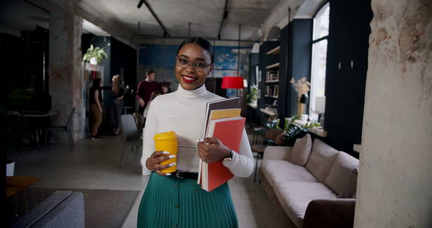 medium portrait of successful young attractive black boss business woman smiling at camera at modern office workplace. - environmental portrait imagens e fotografias de stock