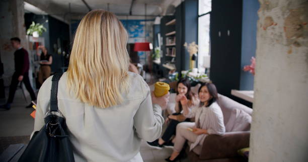 istock Camera follows confident successful young blonde female boss entering multiethnic loft office team meeting with coffee. 1261146549