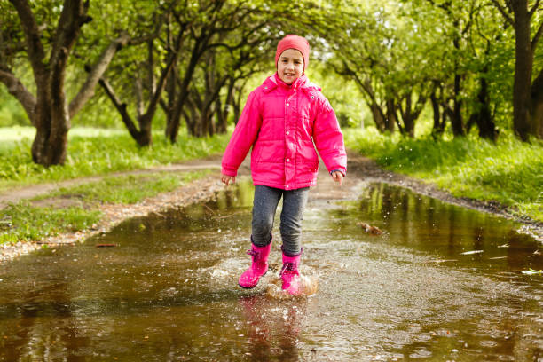 istock cute little girl wearing rain boots jumping into a puddle 1261163113