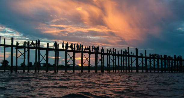 Sunset pink and blue color over U Bein Bridge. At sunset Buddhist monks and people cross U Bein Bridge, returning home u bein bridge stock pictures, royalty-free photos & images
