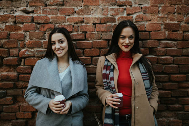 istock Two women standing against red brick wall holding coffee cups 1261221566