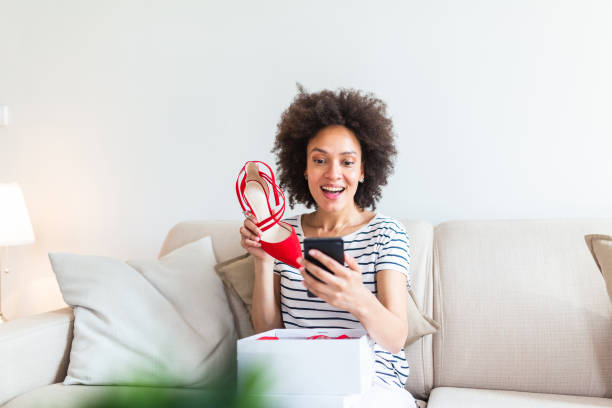 istock Smiling woman unboxing a postal parcel and taking a selfie with her new purchases using a smartphone. Showing shoes to her friends via video call 1261223233