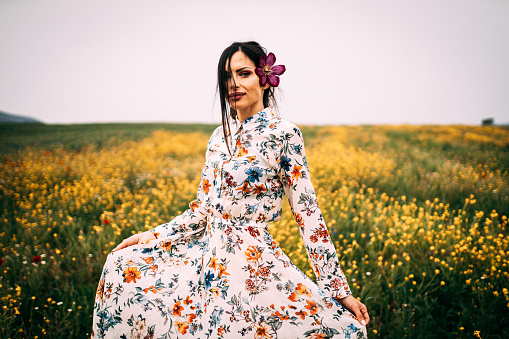 Beautiful young woman with a flower in her hair wearing floral pattern dress enjoying a sunny summer day in the flower field
