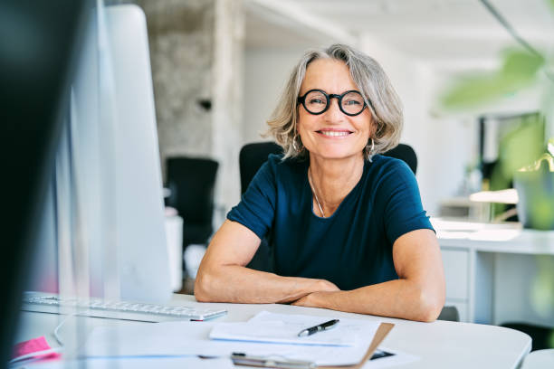 glimlachende onderneemster bij bureau in bureau - mature woman stockfoto's en -beelden