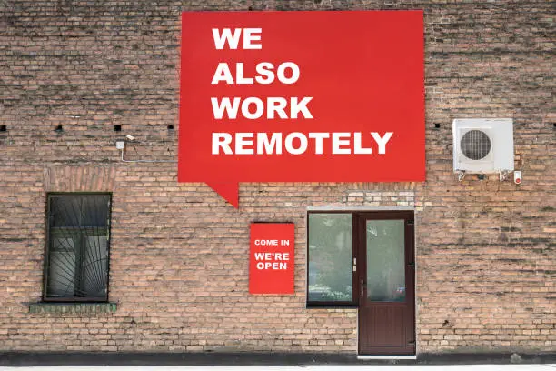 Photo of WE ALSO WORK REMOTELY. COME IN WEâRE OPEN. Advertising banner and information on the wall. Sales and service