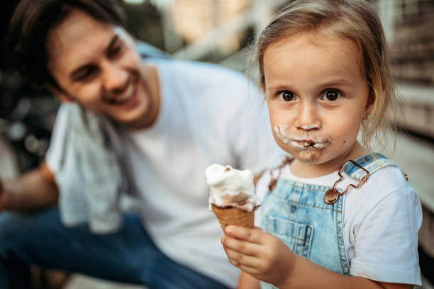 Messy girl Father and daughter licking ice cream in public park licking ice cream cone stock pictures, royalty-free photos & images
