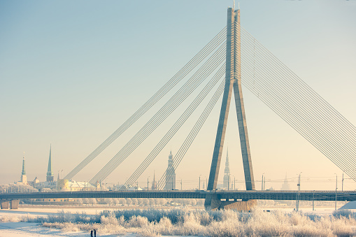 Cable-stayed bridge in Riga in winter against the background of the city panorama. Buildings and trees are covered with white frost. Sunny winter day
