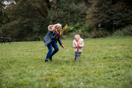 A woman chasing her young daughter while playing tag in Jesmond Dene Park, Newcastle-Upon-Tyne.
