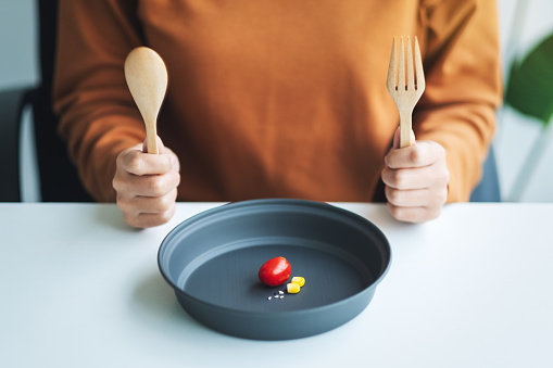Closeup image of a woman holding spoon and fork to eat small amount of food for diet concept