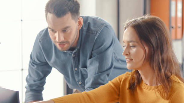 istock Portrait of Beautiful Female Office Employee Working on Computer, Handsome Project Manager Stands Beside and gives Advice on Optimizing Workflow for Customer Experience Management 1261396361