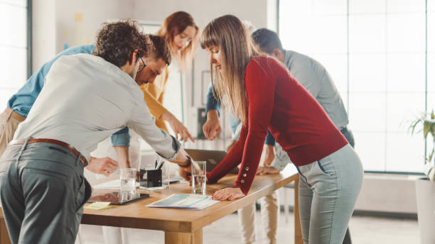 istock Startup Meeting Room: Team of Entrepreneurs Standing Around Conference Table Have Discussions, Solve Problems, Use Digital Tablet, Laptop, Share Documents with Statistics. 1261396911
