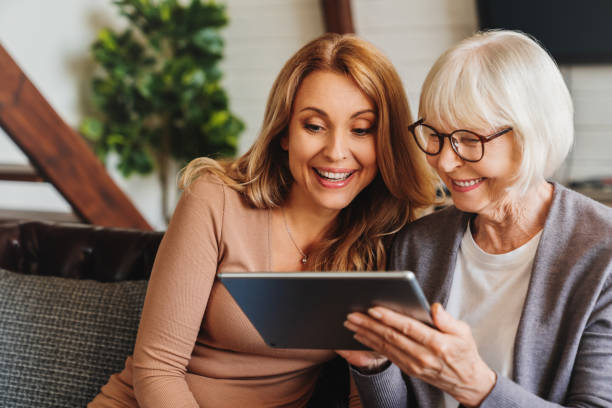donna anziana positiva e sua figlia che usano il tablet a casa - grandparent adult smiling looking at camera foto e immagini stock