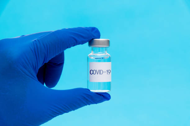 istock Hand holding a Covid-19 vaccine vial on blue background 1261421922