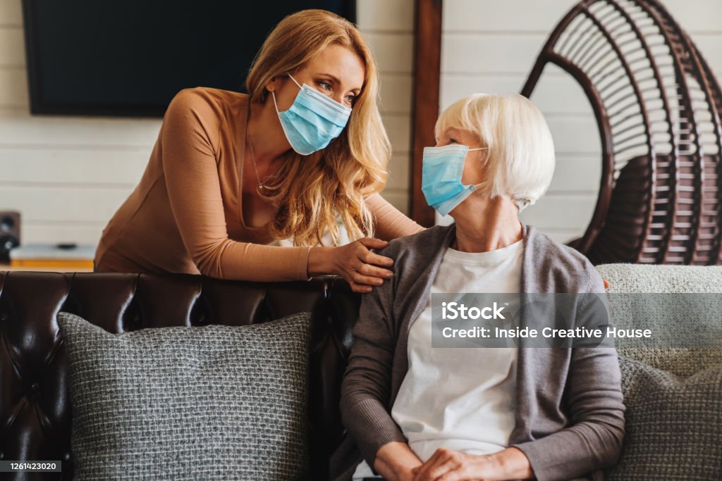 Seniorin in medizinischer Maske mit Sozialarbeiterin zu Besuch zu Hause - Lizenzfrei Schutzmaske Stock-Foto