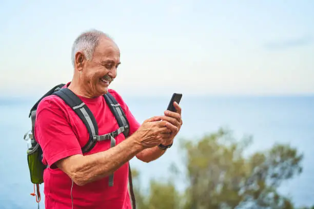 Photo of Smiling senior man using his phone gps while out hiking