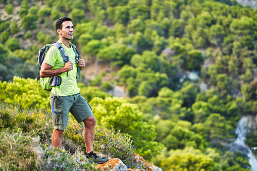 Man wearing a backpack standing on a rocky outcrop and looking at the view during a lone hike in the hills