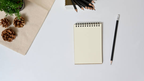 istock Cropped shot view of workspace with blank notebook, pencil and pine cone on white background in office. Top view 1261475599