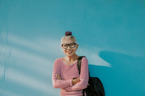 The smiling face of Thai senior unique fashionable woman with a blue wall in the morning