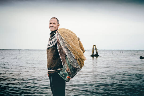 Shrimp fisherman setting out his nets in the sea. Candid portrait of a shrimp fisherman preparing his nets in the shallow water. Colour, horizontal with some copy space. The net is left in the water for 24 hours before it is hauled in and the catch sorted. Photographed on the island of Nyord in Denmark. He is fishing for salt water shrimp in the local fjord’s and they are highly sought after as a delicacy here in Denmark. fisherman photos stock pictures, royalty-free photos & images