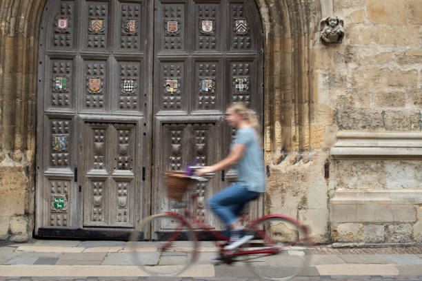 estudiante femenina montando bicicleta de moda antigua alrededor de oxford university college buildings con motion blur - oxford fotografías e imágenes de stock