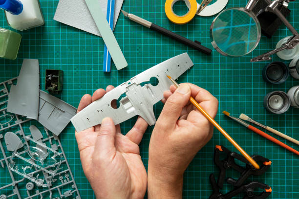 Overhead View Of Man Building Scale Model Aeroplane From Kit On Cutting BoardWith Tools And Materials