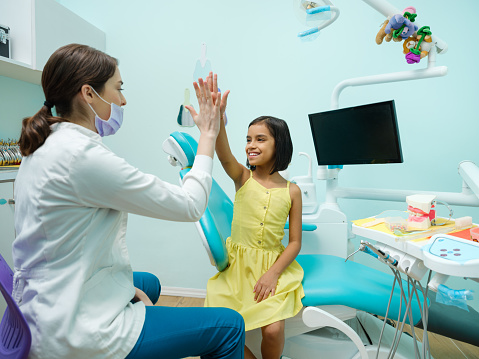 A cute latin girl sitting and giving high-five to dentist in a dental office.