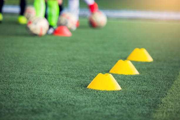 istock selective focus to red cone marker is soccer training equipment on green artificial turf with blurry kid players training background. 1261509662