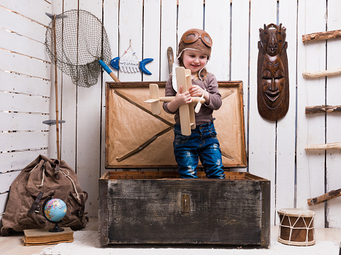 cute little girl in chest with wooden plane in hands in decorated room