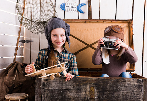 two little girls-pilots in big wooden chest playing camera and wooden plane