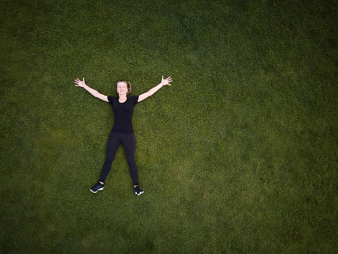 Top view of a woman lying on a green grass filed with arms spreaded