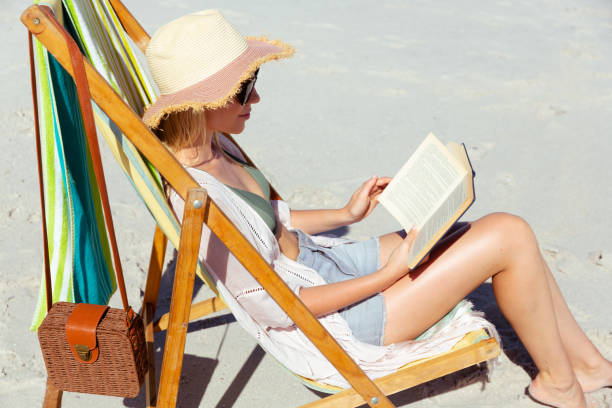 istock Woman reading a book while sitting on the beach 1261549717