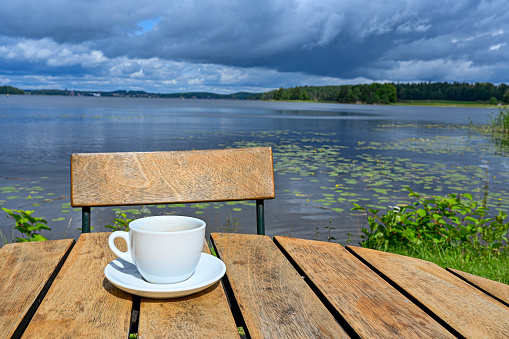 coffee cup on wooden table near lake with cloudy sky