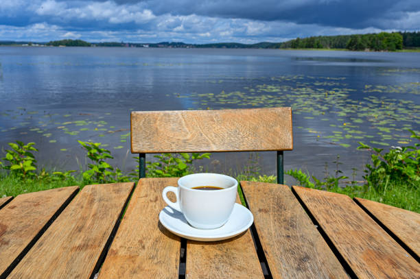 coffee cup on wooden table near lake with cloudy sky
