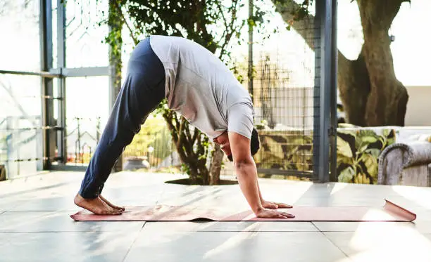 Photo of Young man practicing the downward facing dog pose in a yoga studio