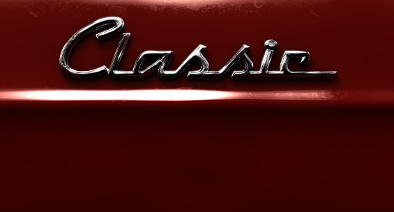 A closeup view of the word classic written as a chrome emblem in a retro font set on a car painted in reflective red paint - 3D render