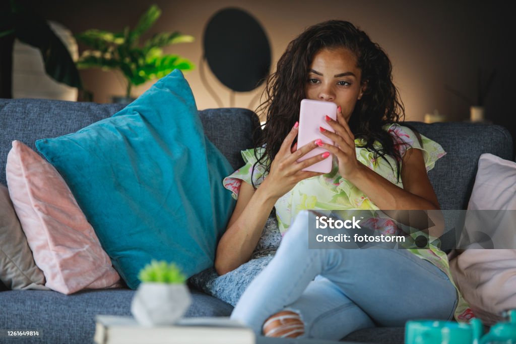 Checking notifications from all the social networks before going back to daily duties Front view of adult woman sitting on her living room while checking her messages and notifications from social networks like Facebook, Whatsapp, Viber, Telegram, Instagram and Linkedin. African Ethnicity Stock Photo