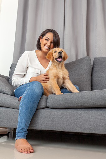 Woman sitting together with her young dog on sofa at home