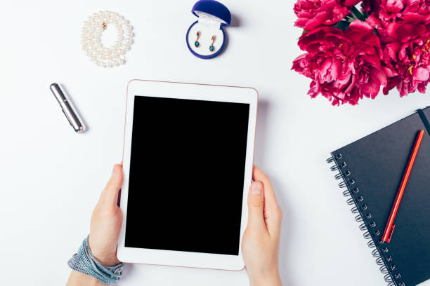 Woman's hands holding digital tablet with blank screen next to notepad