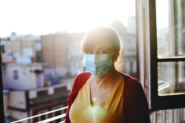 istock woman wearing face mask at the window 1261658362